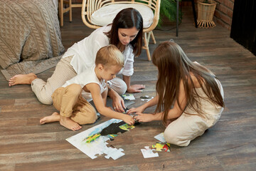 Mom daughter and son put the puzzle together on the floor. Family entertainment. Woman girl and boy...
