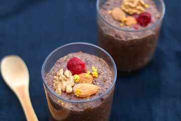 Two glasses of chocolate, orange and chia seed pudding with nut and raspberry topping. Selective focus, dark blue background.