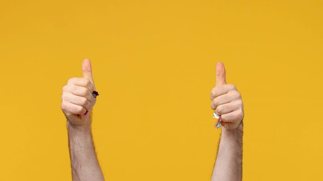 Flying falling colorful confetti isolated over yellow orange background studio. Holiday party birthday lifestyle Happy New Year concept. Cropped close up Man toss up golden shine tinsel show thumbs up