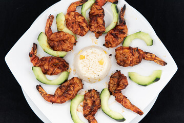 Overhead view of shrimp zarandeado arranged in perfect presentation and garnished with sliced cucumbers on a plate
