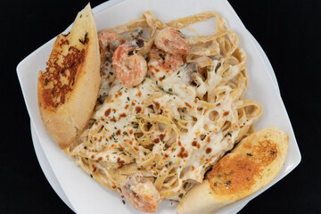 Overhead view of Mexican culinary favorite seafood pasta garnished with garlic bread on a plate.
