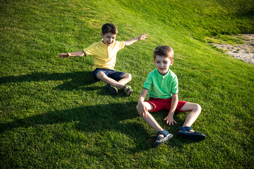 Two Young boy sitting on the grass. Kid are best friends brothers relaxation on nature enjoy warm summer day