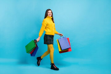 Full length photo of pretty sweet young lady wear yellow sweater walking holding shopping bargains...
