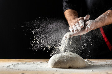 Beautiful and strong men's hands knead the dough make bread, pasta or pizza. Powdery flour flying...