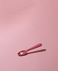 Pink , plastic spoon with heart on pink pastel background. Creative, minimal concept.