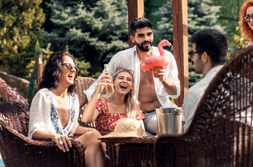 Group of young people having fun at summer vacation and enjoying a poolside party with drinks.