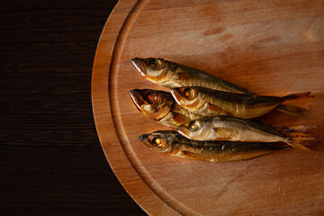 five small smoked goldfish mackerel fish on a wooden round board on a black wooden table...