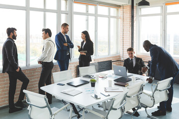 Mature businessman to discuss information with a younger colleague. People working and communicating while sitting at the office desk together with colleagues sitting.