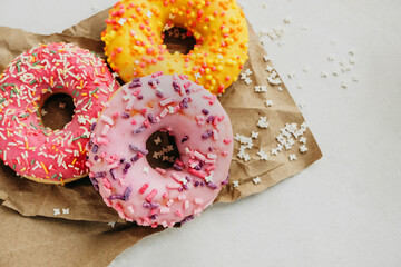 three tasty multi-colored pink and yellow very appetizing glazed donuts on kraft paper for delivery, vertical food content, selective focus