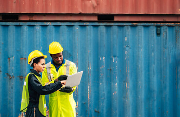workers teamwork man and woman in safety jumpsuit uniform with yellow hardhat and use laptop check container at cargo shipping warehouse. transportation import,export logistic industrial service