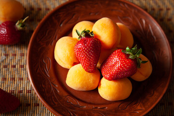 composition with a fruit plate on light brown horizontal striped table. The fruit as a whole. Assorted apricots, strawberries on a round clay brown plate. Vegetarian menu. raw food. healthy food.