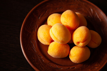 large horizontal photo. background. many fresh ripe orange apricots on a brown clay plate on a background of a dark wooden table. sunny summer day