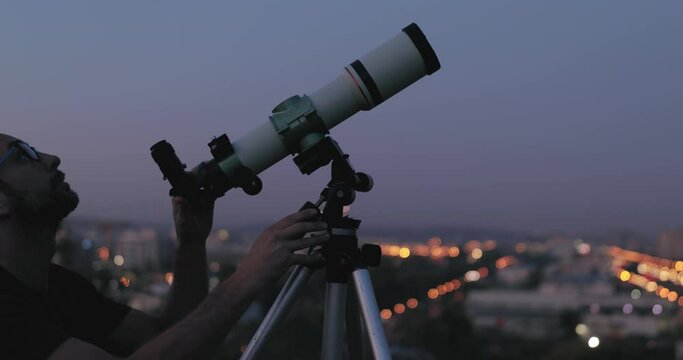 Amateur astronomer looking at the stars with a telescope with blurred city lights in the background.	
