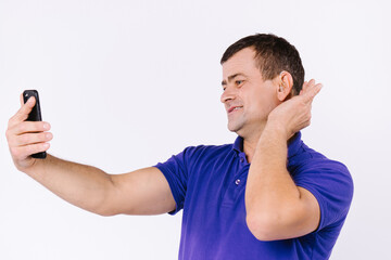 Senior man with a hearing aid and casual clothes communicates on the phone on a white background.