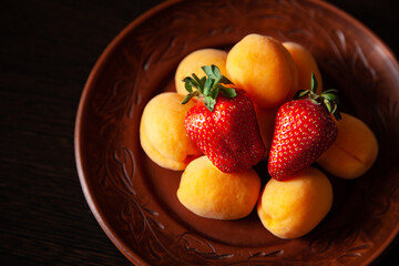 Summer fruits and berries. Ripe apricots and strawberries on a brown clay plate. close-up.