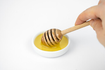 Liquid honey pouring with wooden stick in small white plate.