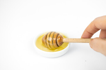 Liquid honey pouring with wooden stick in small white plate.