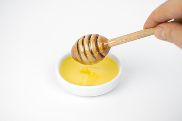 Liquid honey pouring with wooden stick in small white plate.