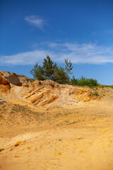 vertical photo. mountain of pressed sand. pattern on a slice of a sandy mountain. wild nature. minerals. summer time. sunny day. sand quarry. horizon with clear blue sky and trees on the mountain.