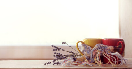 red and yellow cups are wrapped in a purple scarf and decorated with a lavender bouquet against the background of the window. date with the aroma of coffee