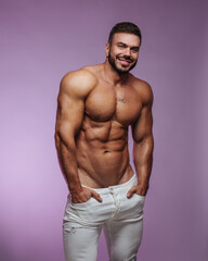 Fototapeta premium Male fitness model in white jeans standing at pink background