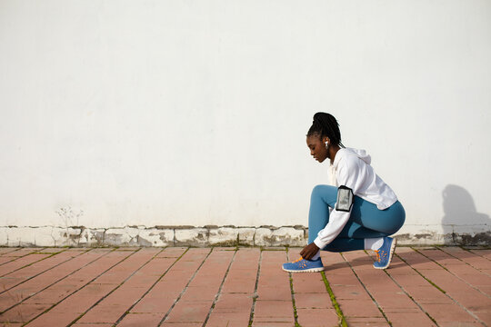 Side View Of Urban Female Runner Getting Ready For Training Outside. Sporty Young Black Woman Looking At Camera While Lacing Her Running Shoes. Fitness Lifestyle And Motivation.