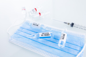 Vials of COVID-19 vaccines are placed on a medical mask, and next to it is a bottle of coronavirus
