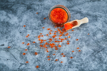 A jar of red caviar and wooden spoon on marble background