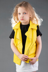 Beautiful little blonde girl in a yellow jacket on a gray background. Five year old girl. Model tests for a child.