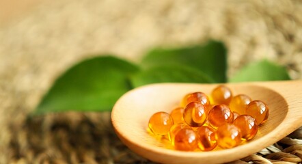 Healthy Vitamins Omega 3 fish liver oil capsules in wooden spoon. Golden translucent pills on background of green leaves. Healthy every day fatty acids nutritional supplement. Copy space, close up