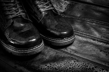 Black wet boots made of genuine leather. Men's shoes with laces with water drops. Fashionable style. On a dark contrasting leather background. Black and white image.