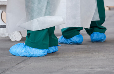 Close up feet of health workers in PPE clothing and blue protective plastic bags on the ground during working in outdoor public area