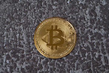 Physical coin with bitcoin cryptocurrency on a gray-brown background.