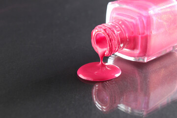 Pink nail polish is poured out of the bottle bottle on a black background with a copyspace place...