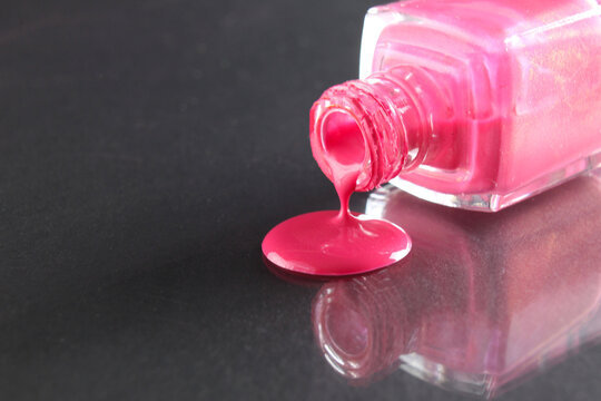 Pink nail polish is poured out of the bottle bottle on a black background with a copyspace place for text