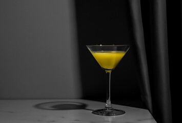 Orange juice or lemon alcohol cocktail in glass on the marble table. Yellow and grey trendy colors of 2021 years still life