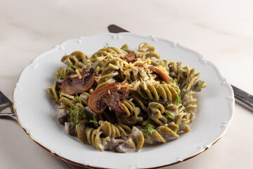 Healthy organic spinach pasta with mushroom and cheese served on a white plate. 