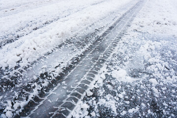 Snow tyre mark. Asphalt covered in snow. Dangerous road conditions. Car imprint on frozen ground. Tire trail on ice. City streets covered in snow during heavy snow fall. Slippery road background.