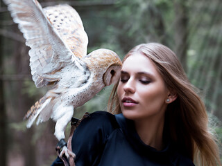Misterioius young blond girl with a barn owl white bird in a foggy forest