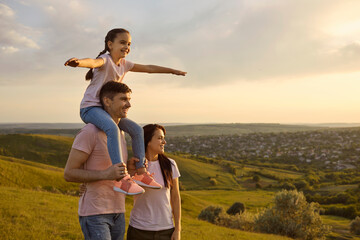 Happy parents with a child on their shoulders play in nature.