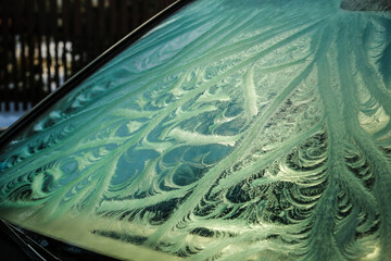 The frozen window of a car in cold winter day. Frost pattern. Selective focus