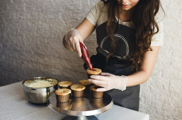 the girl cooks cupcakes at home. Hands of a chef with a pastry bag, squeezing the cream on the cupcakes
