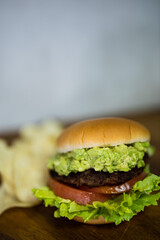 a delicious hamburger and some potato chips. the burger has lettuce, a beef patty, tomato and avocado in them. the buns are freshly baked and it is a very healthy burger. the chips are crisp