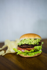 a delicious hamburger and some potato chips. the burger has lettuce, a beef patty, tomato and avocado in them. the buns are freshly baked and it is a very healthy burger. the chips are crisp