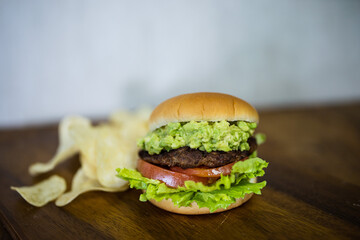 a delicious hamburger and some potato chips. the burger has lettuce, a beef patty, tomato and avocado in them. the buns are freshly baked and it is a very healthy burger. the chips are crisp