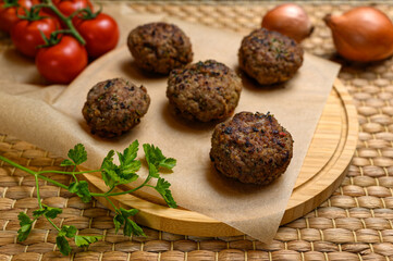 Homemade fried meatballs, served on wooden cutting board with tomatoes, onions and parsley