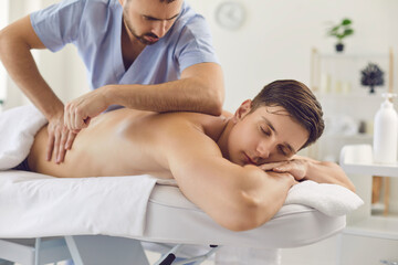 Obraz na płótnie Canvas Man professional masseur in uniform making medical massage of back for relaxing man