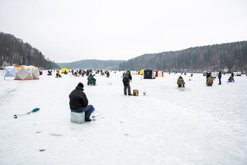 Fishermen fishing on a frozen lake in winter with fishing pole, ice auger and equipment for fishing 