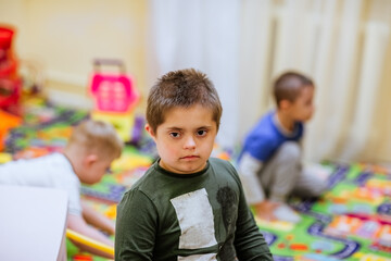 Obraz premium Portrait of young cute boy with Down Syndrome playing in the room.