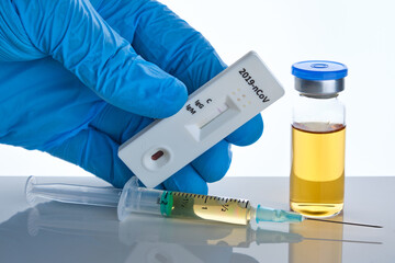 Medical vial vaccine dose with syringe and male doctor hand in blue glove holds corona virus test, white backdrop, selective focus